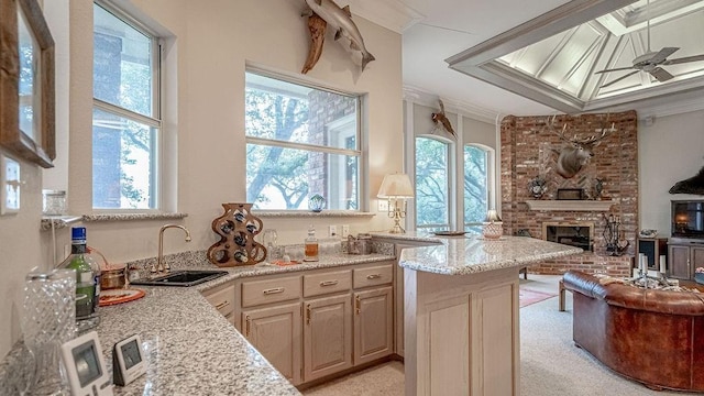 kitchen featuring crown molding, ceiling fan, open floor plan, a fireplace, and a sink