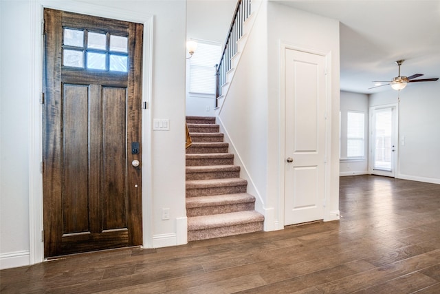 foyer entrance featuring stairway, baseboards, a ceiling fan, and dark wood-style flooring