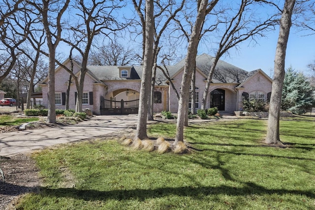 french provincial home featuring brick siding, driveway, and a front yard