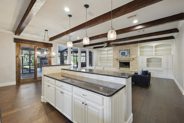 kitchen featuring visible vents, baseboards, dark wood-style flooring, a stone fireplace, and white cabinets