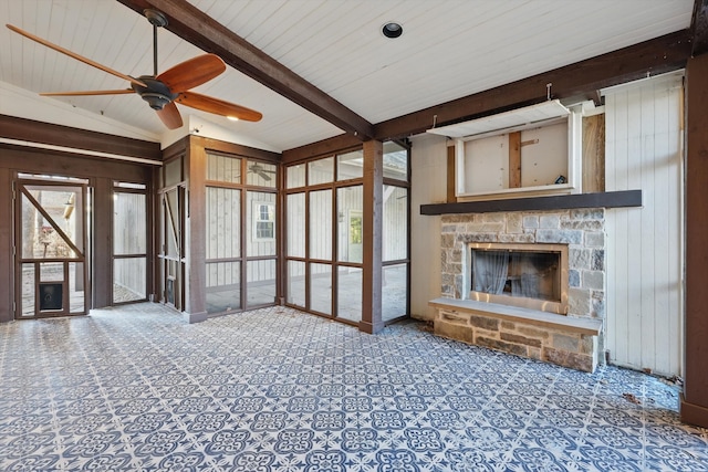 unfurnished living room with a wealth of natural light, wooden walls, vaulted ceiling with beams, and a fireplace