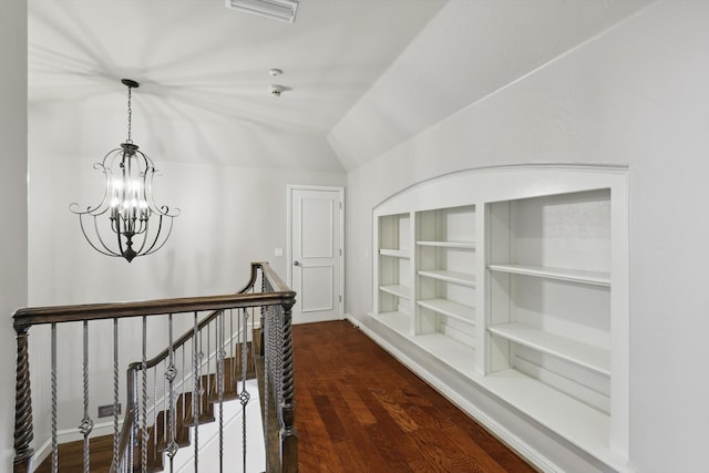 corridor with built in shelves, visible vents, dark wood-type flooring, vaulted ceiling, and an upstairs landing