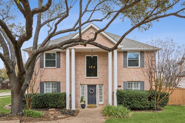 greek revival house with brick siding, a shingled roof, and fence