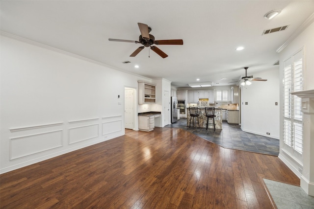 unfurnished living room featuring visible vents, dark wood finished floors, and ornamental molding