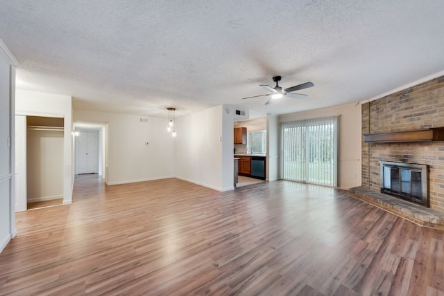 unfurnished living room featuring a textured ceiling, a brick fireplace, light wood-type flooring, and ceiling fan