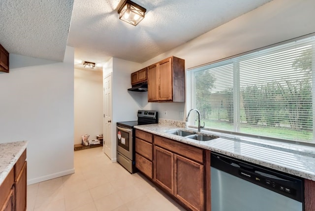 kitchen with under cabinet range hood, brown cabinets, appliances with stainless steel finishes, a textured ceiling, and a sink