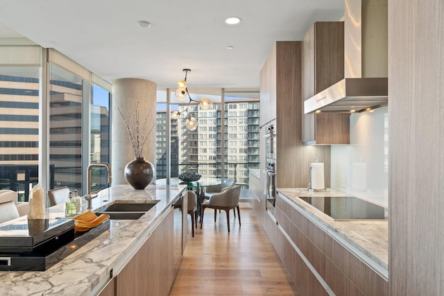 kitchen featuring a sink, wall chimney exhaust hood, black electric cooktop, modern cabinets, and light wood-type flooring