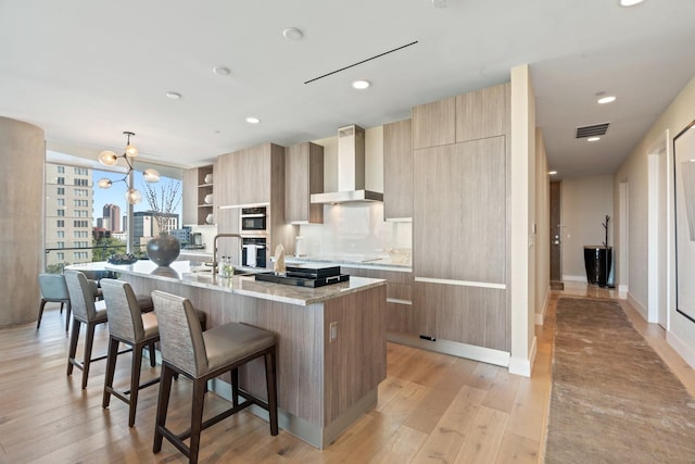 kitchen featuring visible vents, a kitchen bar, modern cabinets, wall chimney range hood, and light wood finished floors