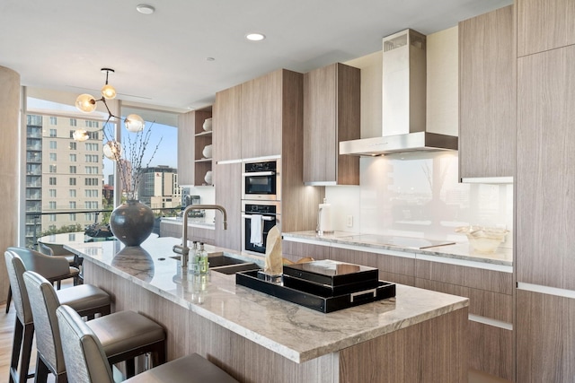 kitchen with wall chimney range hood, a sink, a kitchen breakfast bar, black electric stovetop, and modern cabinets