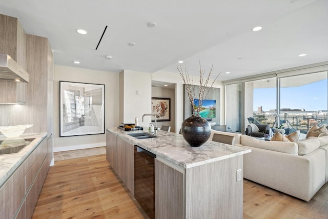 kitchen with modern cabinets, light brown cabinetry, a sink, light wood-style floors, and black electric stovetop