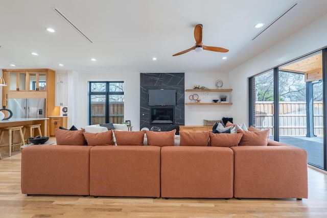 living area featuring recessed lighting, light wood-type flooring, a ceiling fan, and a high end fireplace