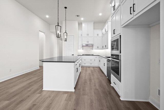 3100 Colt Ln, Celina, TX 75009 - kitchen featuring appliances with stainless steel finishes, wood finished floors, decorative backsplash, under cabinet range hood, and a kitchen island