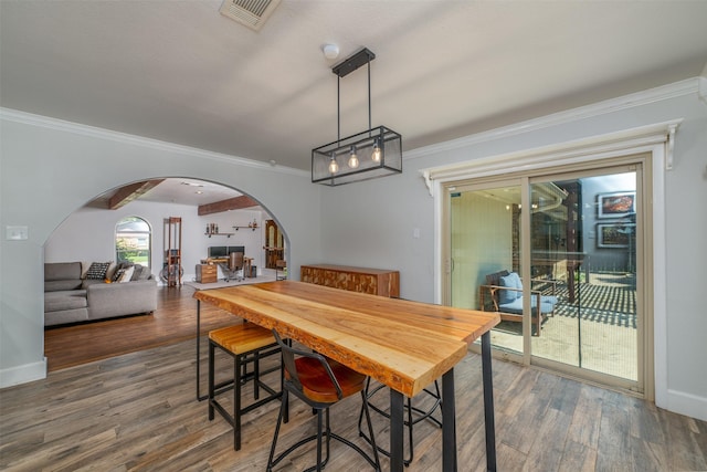 dining area featuring wood finished floors, crown molding, arched walkways, and visible vents