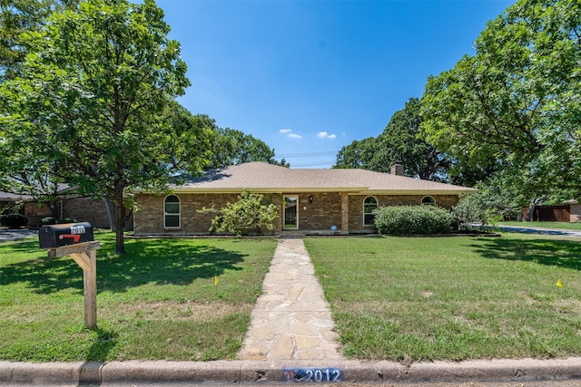 ranch-style house with a chimney, brick siding, and a front lawn