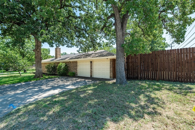 view of property exterior with fence, a chimney, concrete driveway, a garage, and a lawn