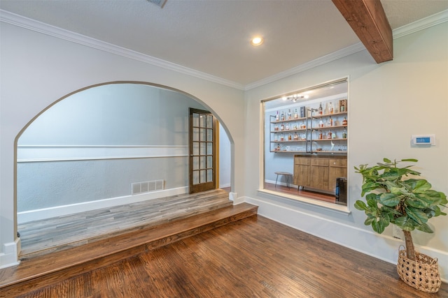 unfurnished dining area with visible vents, wood finished floors, arched walkways, a bar, and crown molding