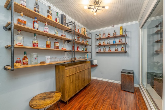 bar with baseboards, dark wood finished floors, a bar, crown molding, and a chandelier