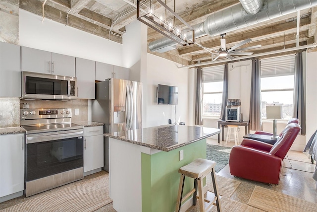 kitchen with a center island, decorative backsplash, appliances with stainless steel finishes, a high ceiling, and a ceiling fan