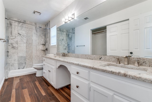 full bathroom with a tile shower, visible vents, wood finished floors, and a sink