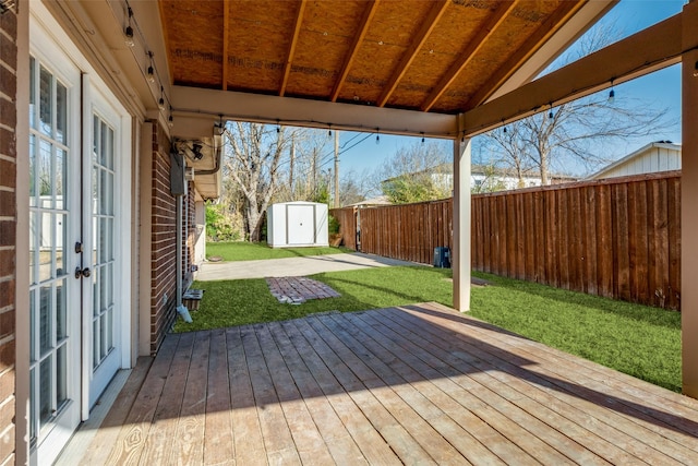 wooden deck featuring an outbuilding, a shed, a yard, a fenced backyard, and french doors