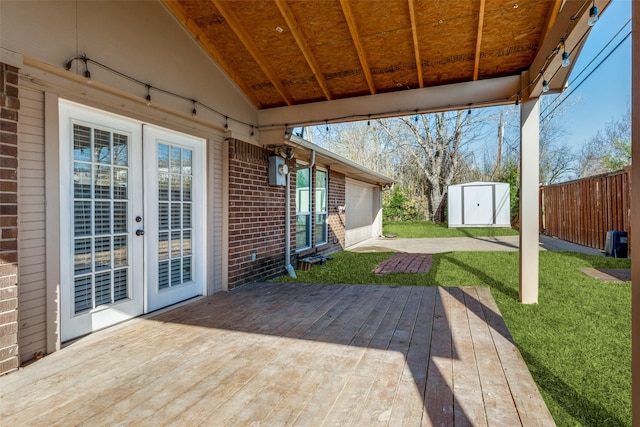 wooden terrace with a storage unit, a lawn, fence, french doors, and an outdoor structure