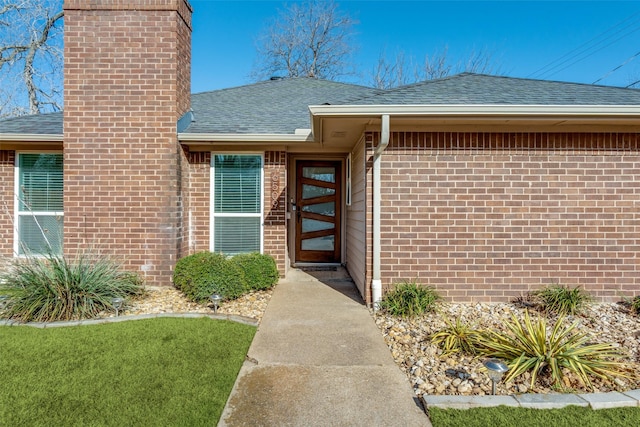 entrance to property featuring brick siding, roof with shingles, and a chimney