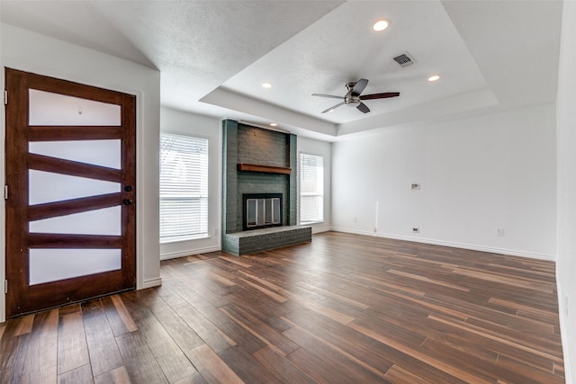 unfurnished living room featuring visible vents, a raised ceiling, dark wood finished floors, and a fireplace