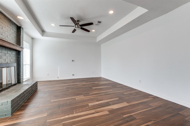 unfurnished living room with visible vents, dark wood-type flooring, a tray ceiling, a fireplace, and baseboards