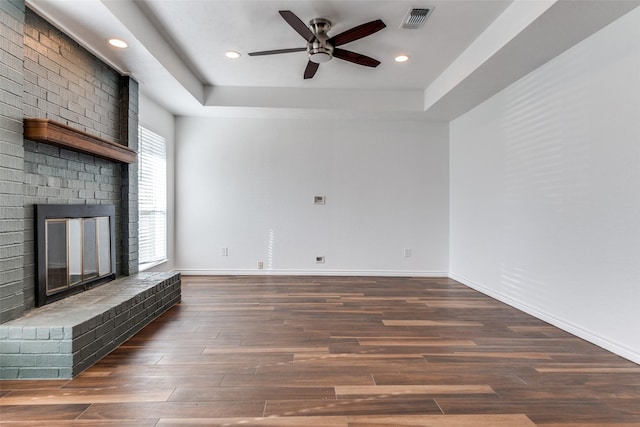 unfurnished living room featuring visible vents, a brick fireplace, baseboards, wood finished floors, and a raised ceiling