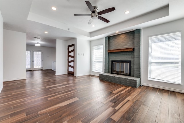 unfurnished living room with a wealth of natural light, a fireplace, a raised ceiling, and dark wood-type flooring