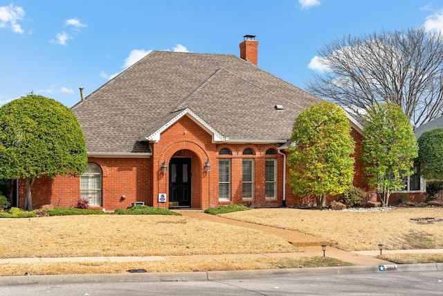 view of front of home with brick siding, a chimney, and roof with shingles