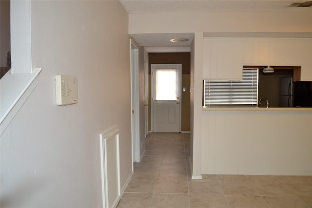 hallway with light tile patterned floors, visible vents, a textured ceiling, and a sink