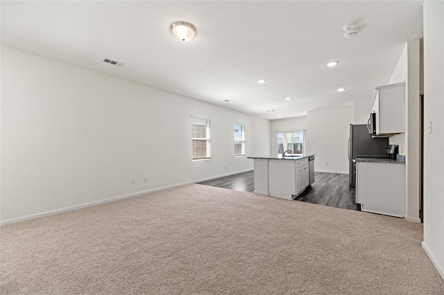 kitchen with a kitchen island with sink, dark colored carpet, dark countertops, stainless steel microwave, and open floor plan