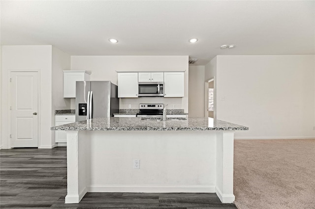 kitchen featuring light stone countertops, a center island with sink, a sink, appliances with stainless steel finishes, and white cabinetry