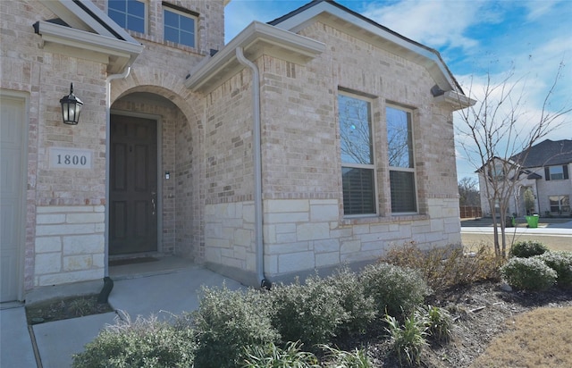 entrance to property with brick siding, stone siding, and an attached garage