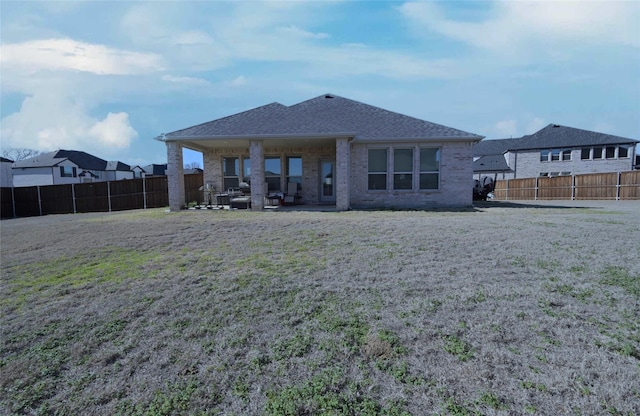 back of property featuring brick siding, a shingled roof, a yard, a fenced backyard, and a patio