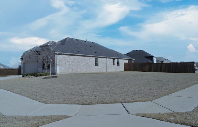 view of property exterior featuring brick siding, a lawn, an attached garage, and fence