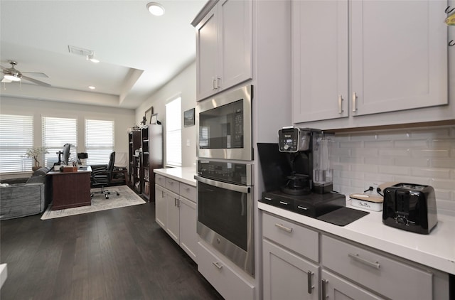 kitchen featuring dark wood-type flooring, stainless steel appliances, light countertops, decorative backsplash, and a raised ceiling