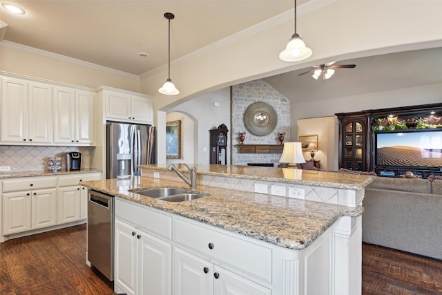 kitchen with a kitchen island with sink, a sink, stainless steel appliances, open floor plan, and a large fireplace