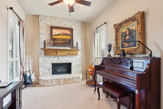 sitting room featuring a stone fireplace, carpet flooring, baseboards, and ceiling fan