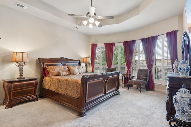 bedroom with visible vents, a raised ceiling, light colored carpet, and multiple windows