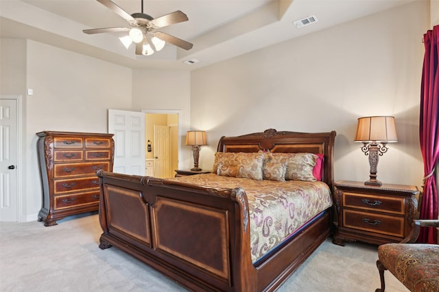 bedroom featuring light carpet, visible vents, a ceiling fan, and a tray ceiling