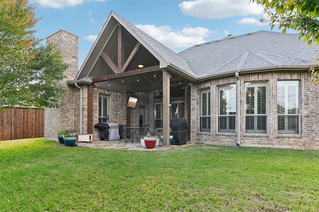 rear view of property featuring a yard, brick siding, a patio area, and fence