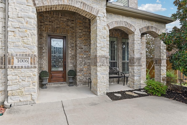 property entrance featuring a porch, brick siding, and stone siding