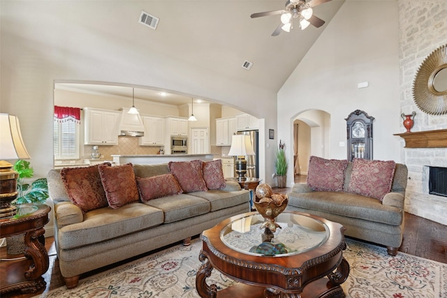 living area with wood finished floors, visible vents, high vaulted ceiling, arched walkways, and a stone fireplace