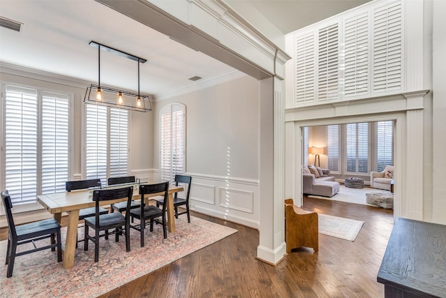 dining room with visible vents, wood finished floors, a decorative wall, wainscoting, and crown molding