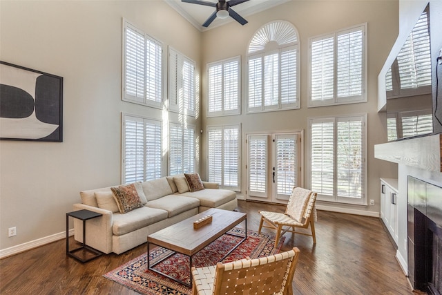 living room featuring dark wood-type flooring, a fireplace, baseboards, and a towering ceiling