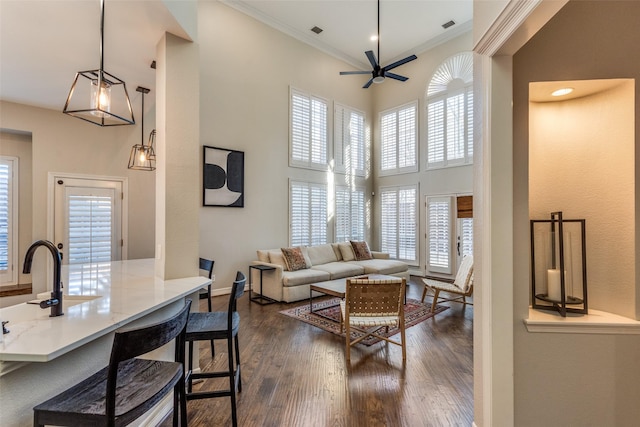 living room featuring baseboards, a high ceiling, ceiling fan, dark wood-type flooring, and crown molding