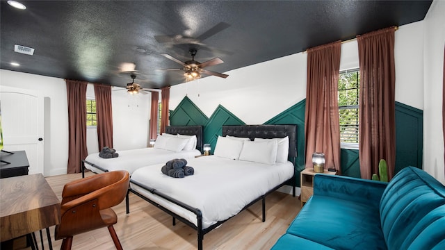bedroom with visible vents, a textured ceiling, light wood-type flooring, and a ceiling fan