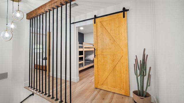corridor with a barn door, beam ceiling, visible vents, and light wood finished floors